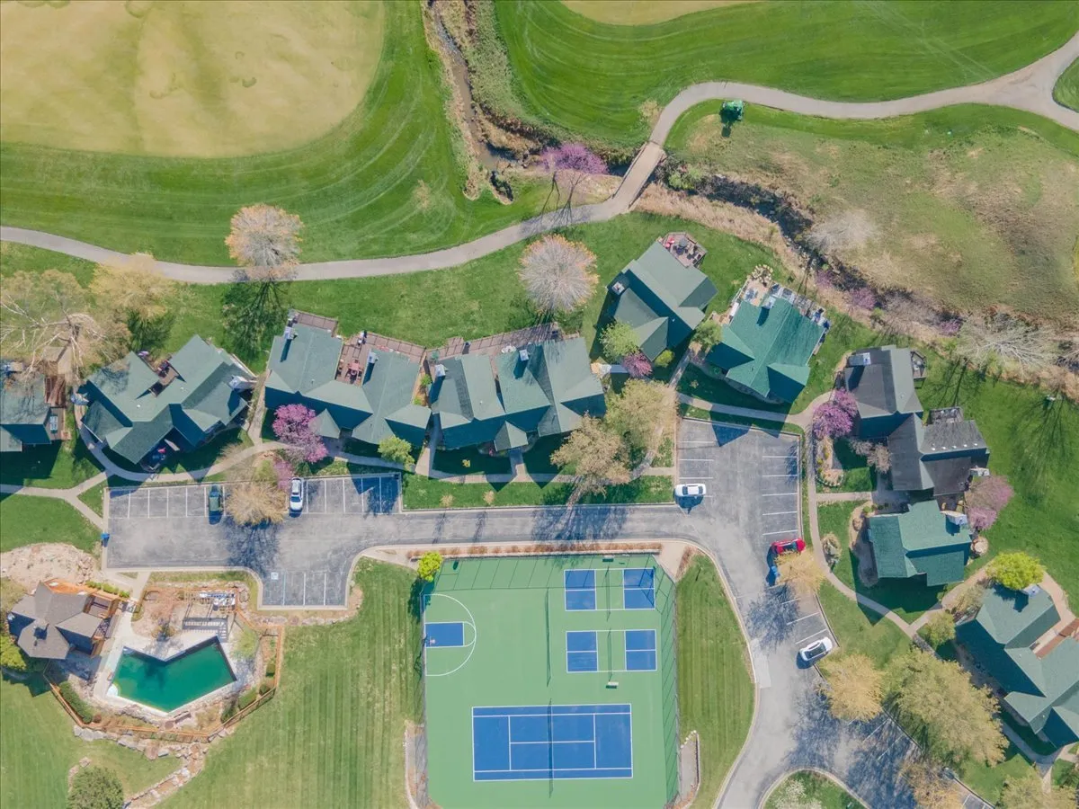 A wide exterior shot capturing the community pool, tennis courts, flowering trees, and well-maintained lawns. The scene is lively and recreational, suggesting quick access to shared amenities and a vibrant community atmosphere just steps from the home.