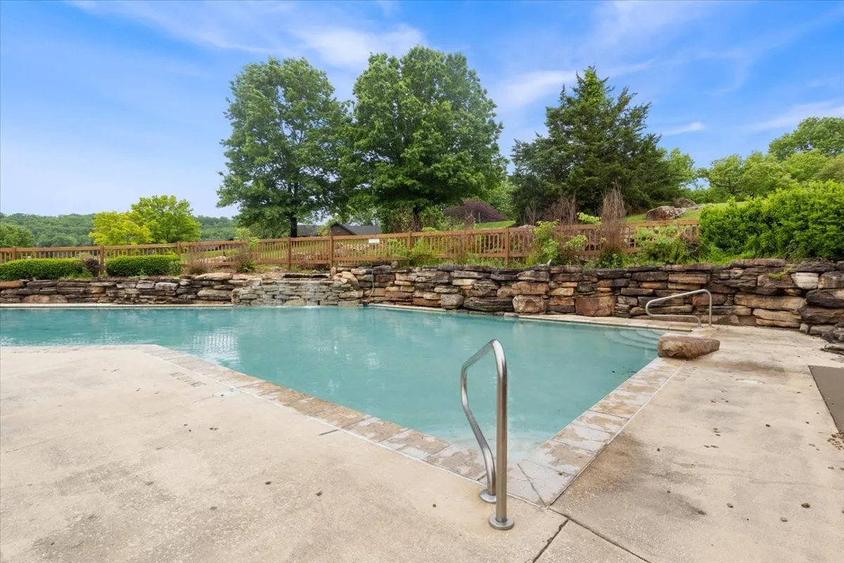 A serene swimming pool surrounded by greenery and a stone wall, bathed in soft light. The calm water and inviting setting evoke relaxation and togetherness, perfect for a quiet afternoon swim or lounging poolside.