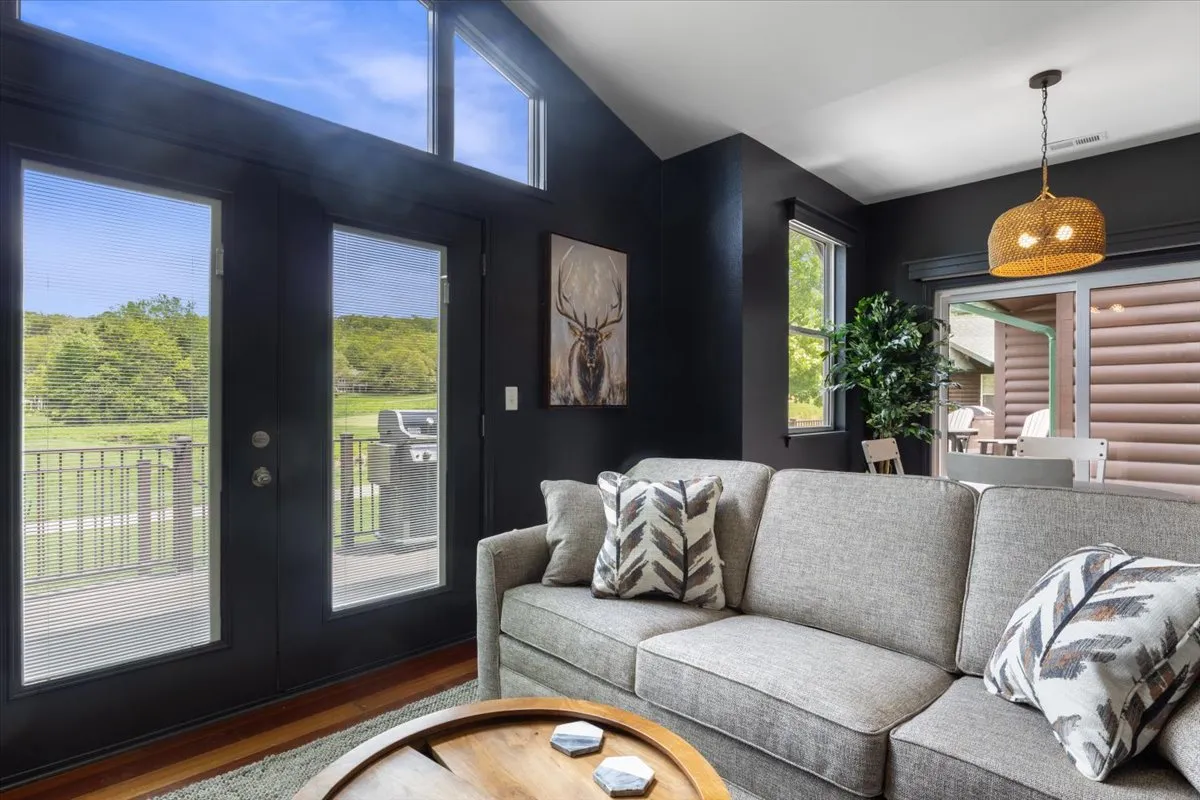 A bright living space with a plush sofa, large windows that let in abundant sunlight, stylish artwork on the wall, and a table with decorative items. The room is styled with contemporary touches and offers a comfortable setting for both relaxation and socializing.