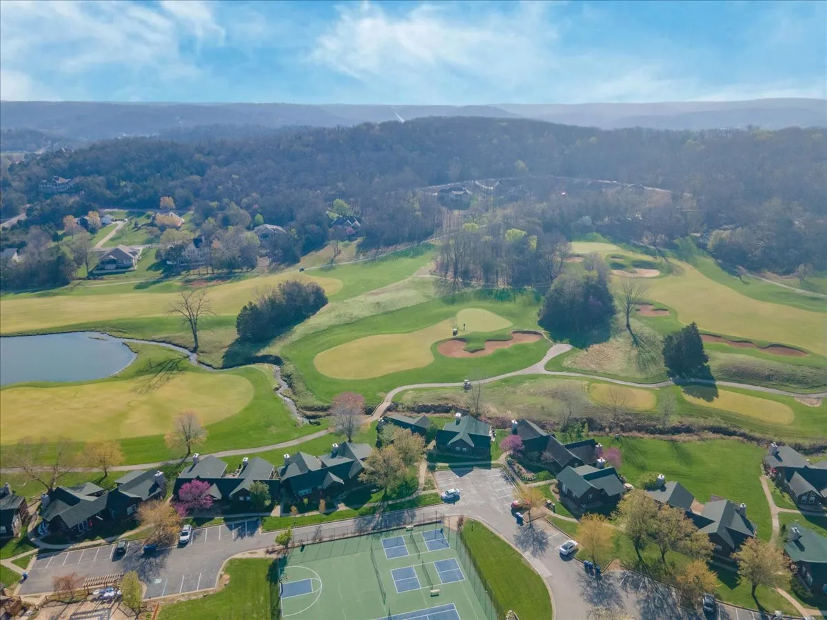 A sweeping view of the golf course bordered by a serene pond, with residential homes and tennis courts visible in the background. The lush greenery and open sky create a relaxed, inviting atmosphere perfect for outdoor group activities.