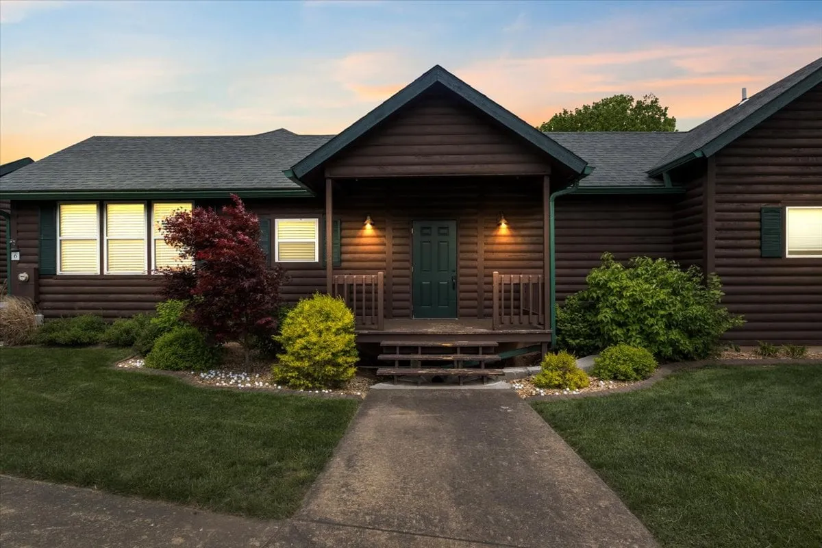 A welcoming entrance with warm outdoor lighting, neatly landscaped walkway, and cozy porch space. The scene evokes feelings of arrival, hospitality, and the start of memorable group experiences.
