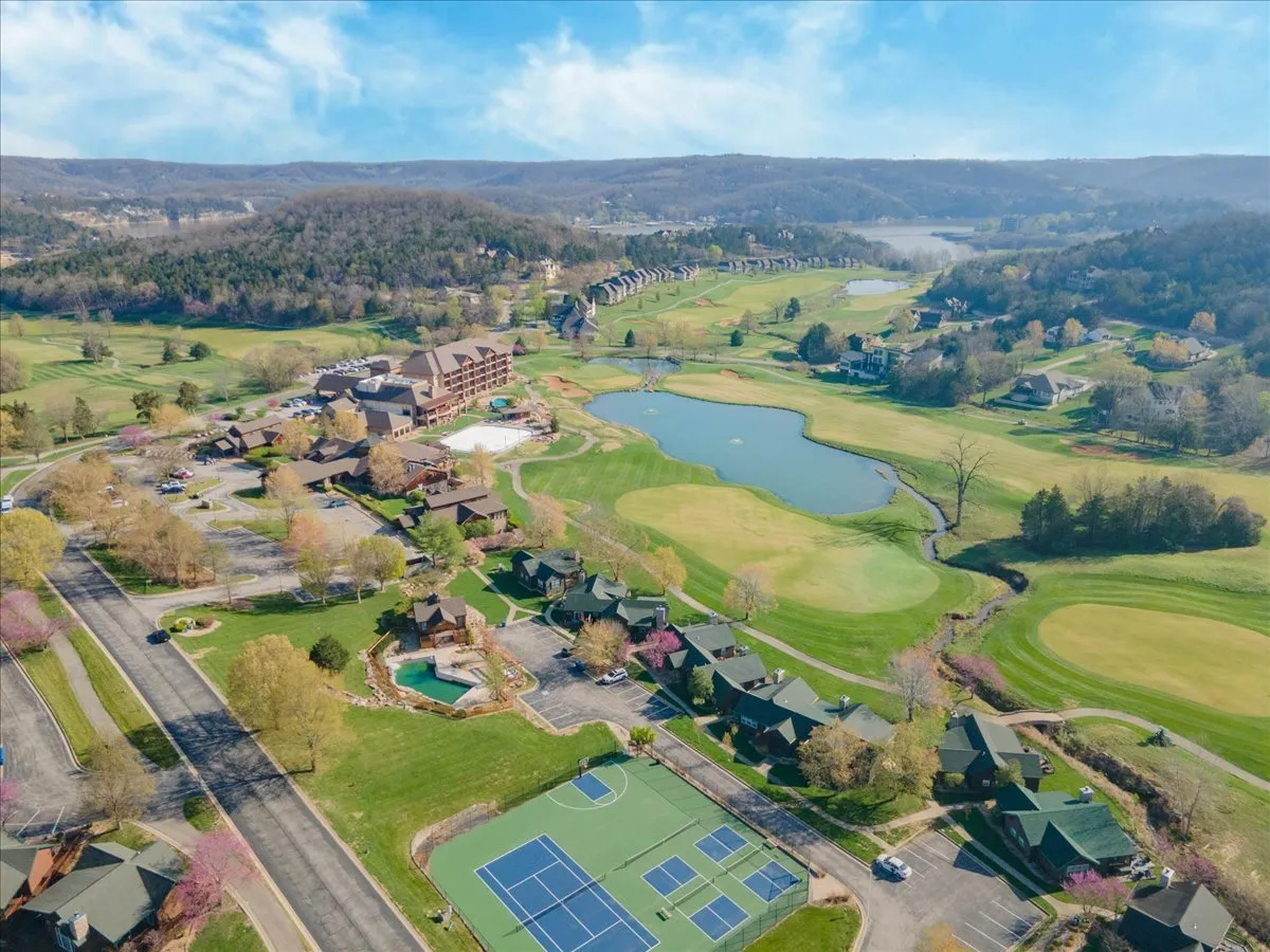 This image shows an expansive view of the Old Kinderhook golf course set alongside a serene lake, with the resort building and tennis courts nestled among lush greenery. The vibrant landscape captures the heart of the property, with golfers visible on the course and recreational amenities clearly in view.