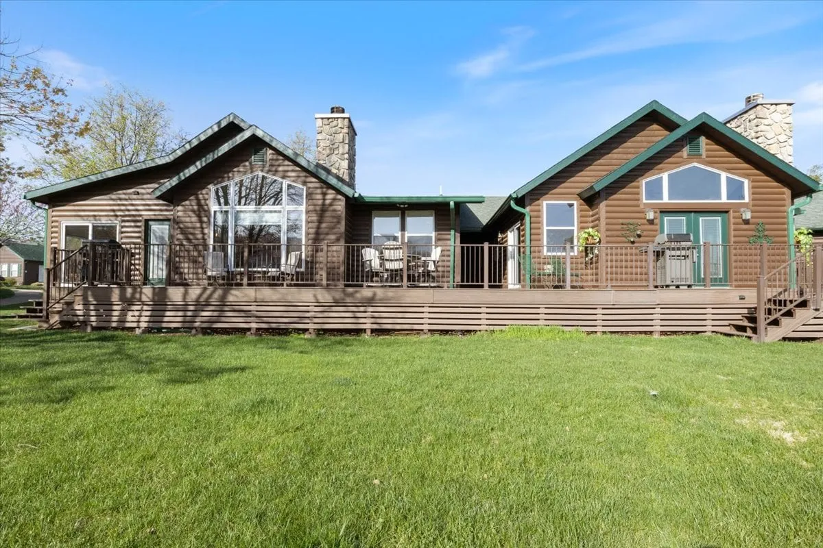 An inviting exterior view that prominently displays a wooden deck overlooking a green lawn, with large windows and stone chimneys in the background. The deck is staged for family gatherings and outdoor dining, and the image is set at sunset, creating a warm, magical ambiance ideal for evening relaxation or entertaining.
