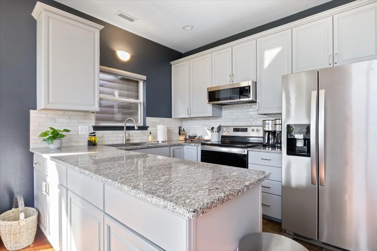 Featuring a granite countertop, stainless steel appliances, rich cabinetry, and a window flooding the kitchen with natural light, this image emphasizes the fully equipped, modern kitchen. The layout is functional for meal prep and entertaining, with a welcoming, modern feel that invites guests to cook and connect.