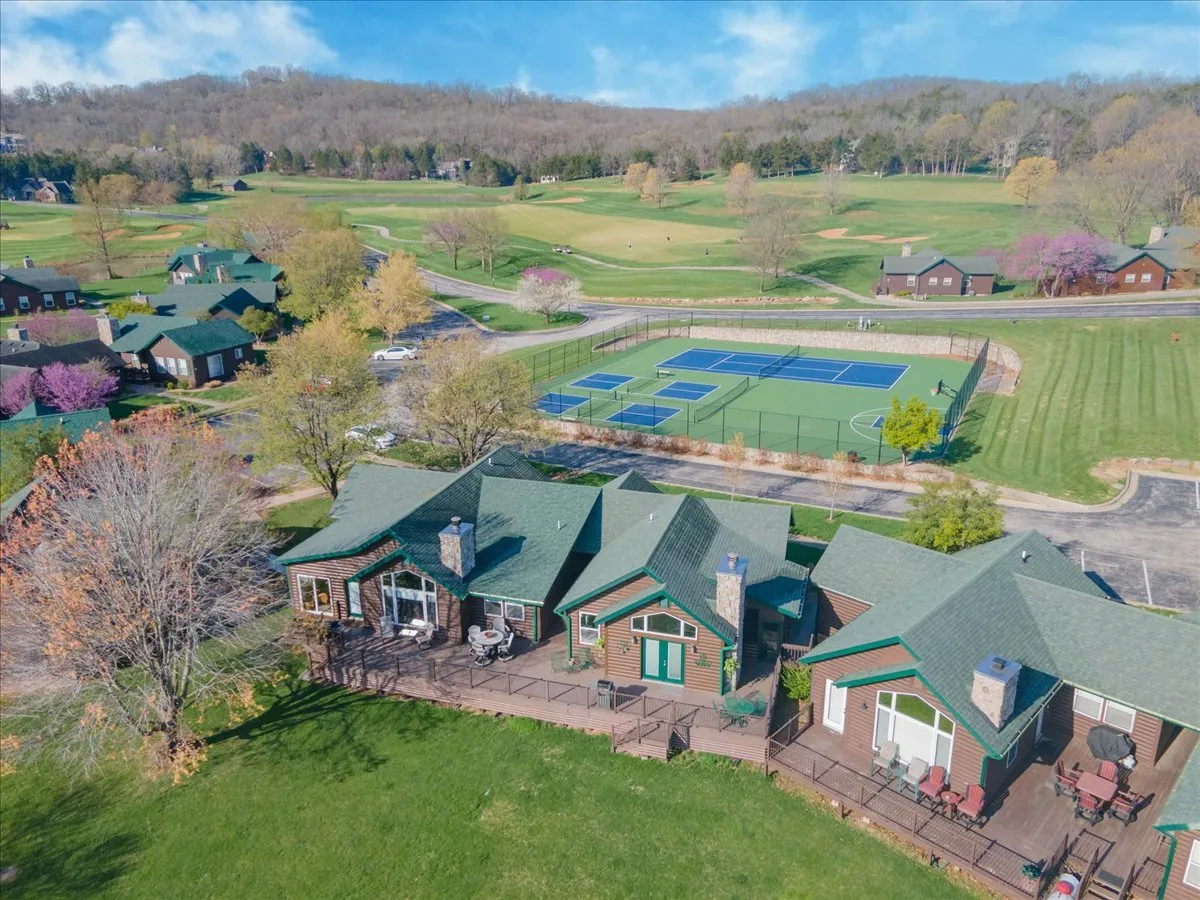 A wide shot featuring green-roofed cabins with porches overlooking both lush golf fairways and well-maintained tennis courts, all framed by blooming trees and vibrant landscaping. The image suggests easy access from the residence to outdoor activities.