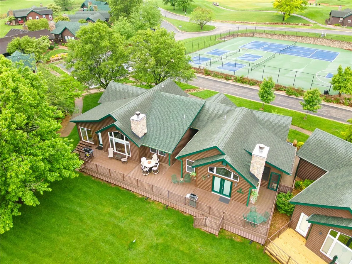 A welcoming deck area with outdoor seating, green roof and siding, and tennis courts in the background. The setting suggests space for outdoor dining, relaxation, and engaging in sports activities.