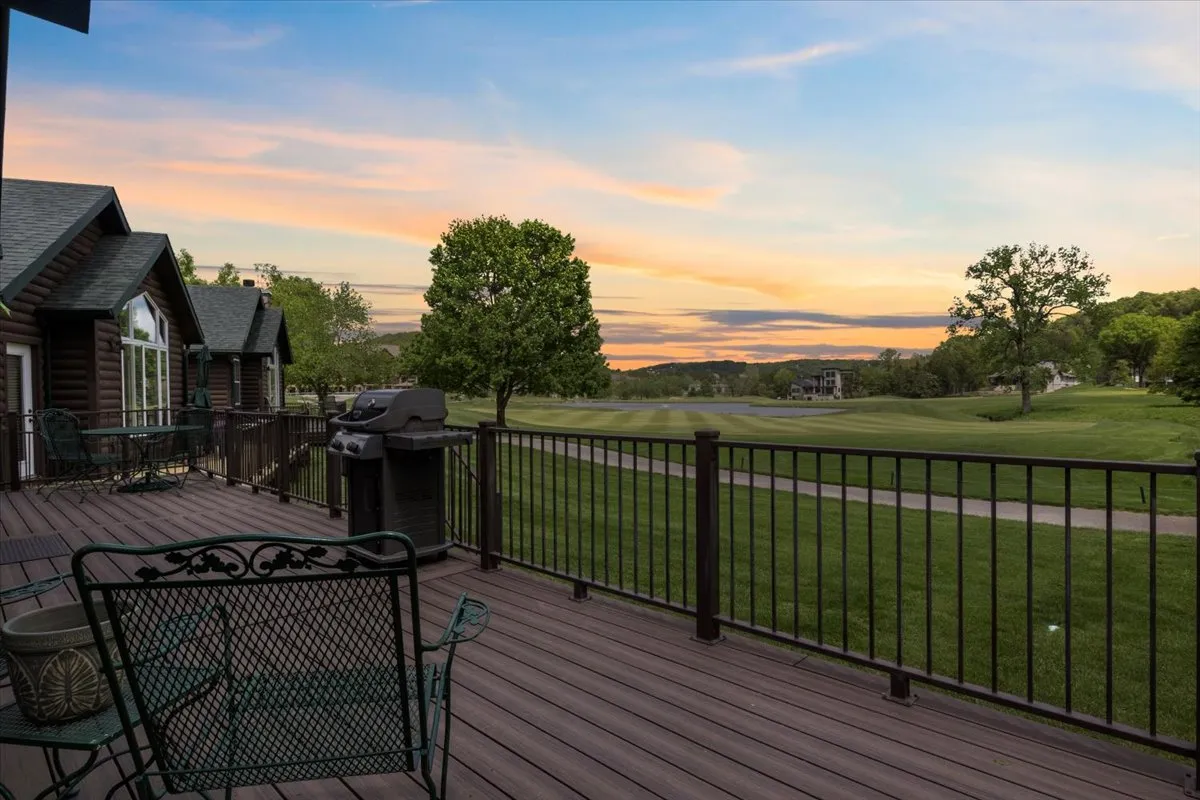 The image showcases the inviting deck of a remodeled cottage overlooking a lush golf course, with a grill ready for barbecuing, comfortable outdoor seating, and a breathtaking sunset sky casting a warm glow over the scenic landscape.